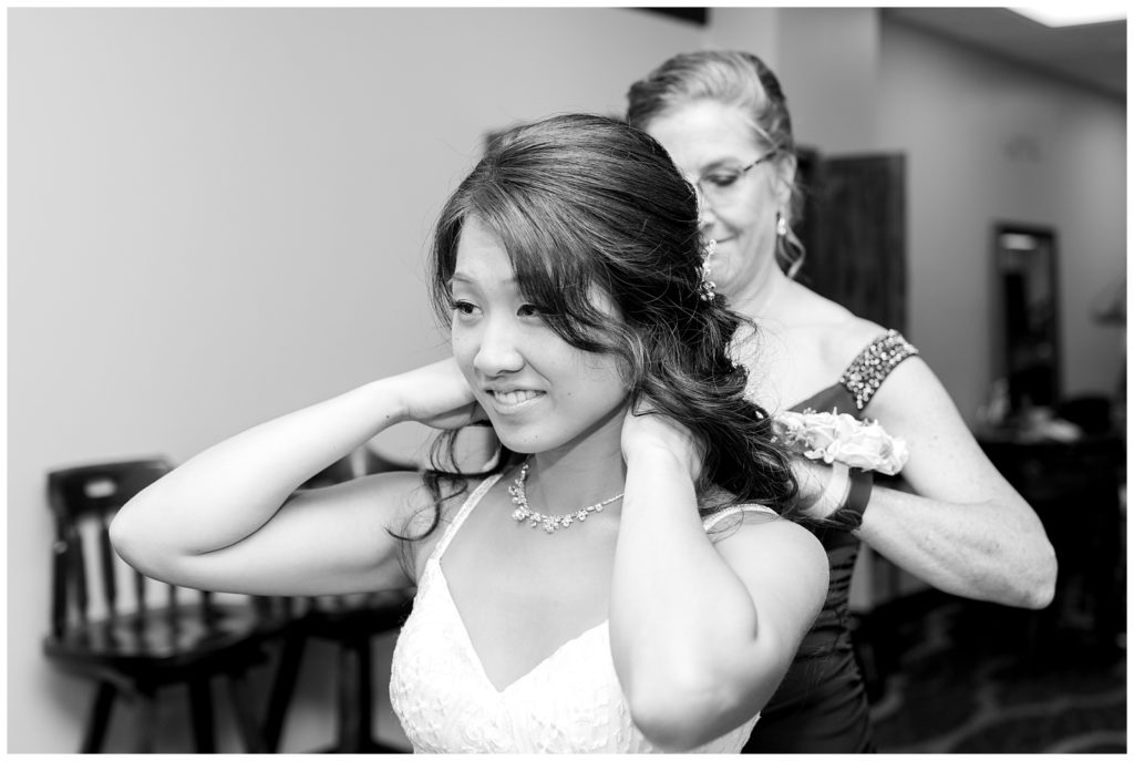 mother of the bride helping her daughter fasten her necklace on her wedding day 